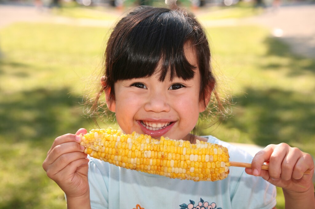 Girl smiling and eating a sweetcorn on a stick 