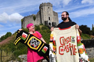 A picture of the wrestler Drew McIntyre and a person from the knitting group Twin Made holding a jumper with the words Clash at the Castle on it