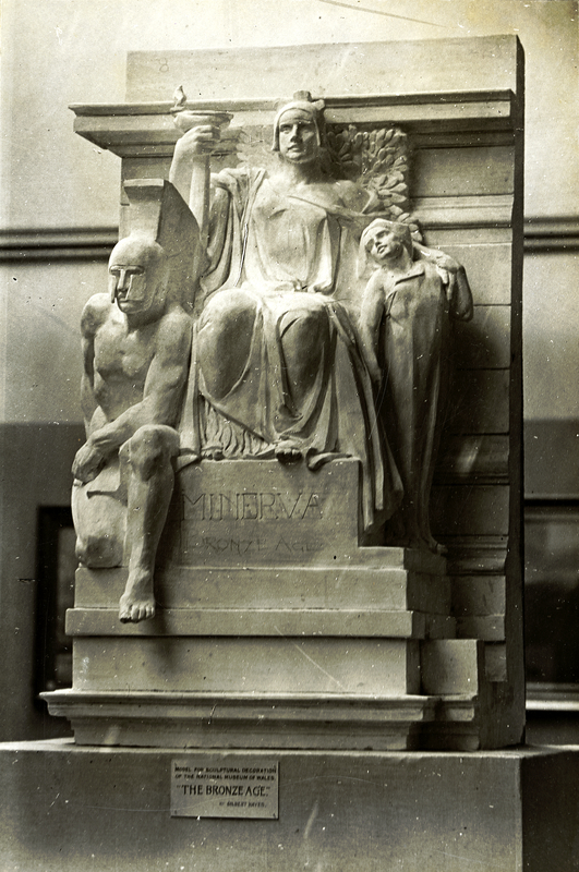 Sepia photograph of a relief sculpture of Minerva seated on a throne, flanked to the left by a muscular man wearing a helmet and a loincloth and to the right by a female figure