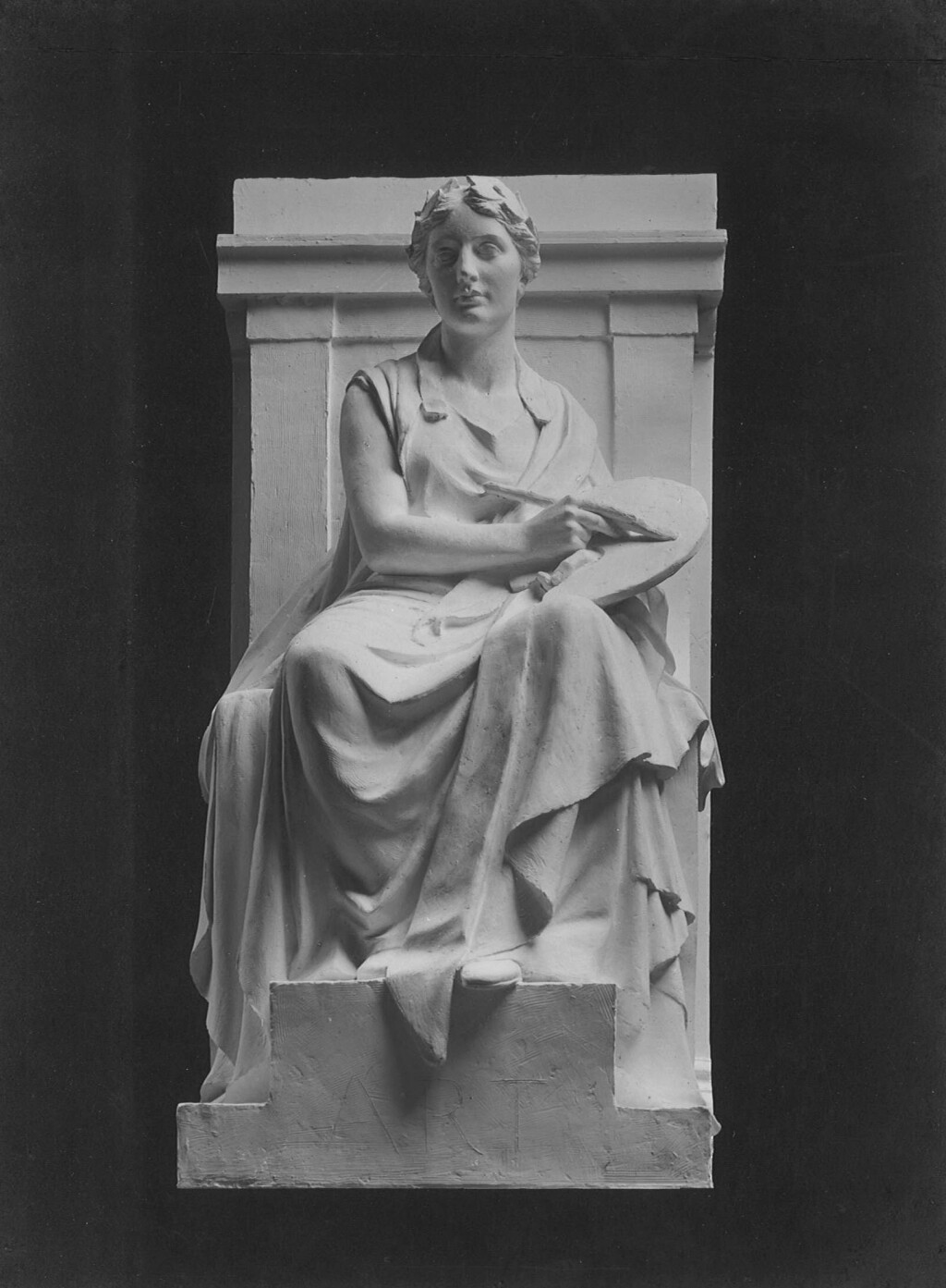 Black-and-white photograph of a plaster model showing a seated woman in an architectural setting holding a palette and paintbrush, against a black background