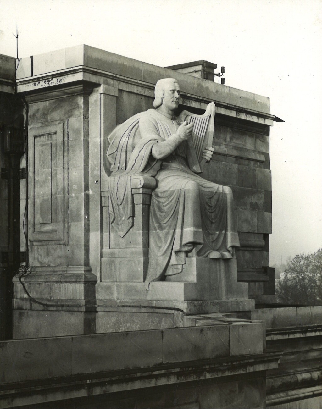 Black-and-white photograph of a stone sculpture of a seated man playing a small harp, set into the architecture of a building