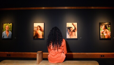 A woman in a dark room, featuring photographs of black people, each with a tattoo