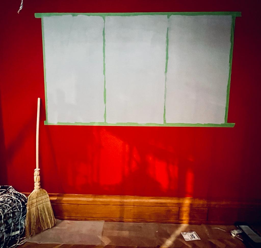 A wall painted red with three white rectangles where film will be projected onto. A broom sits in the left hand corner