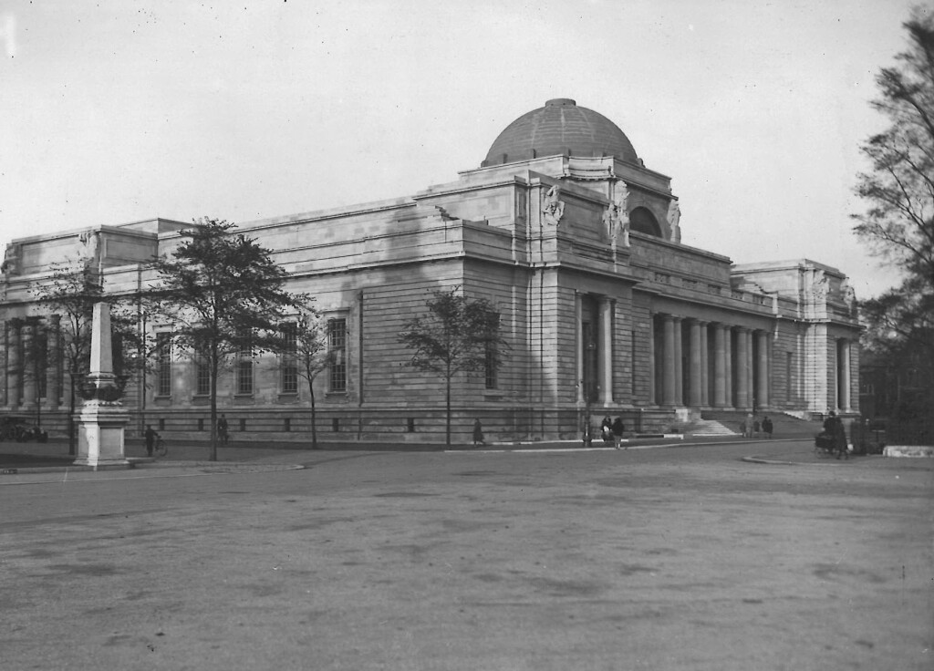 Photograph of the exterior of the National Museum taken from the south-west. A few trees are in the foreground and one or two people can be seen walking around the building