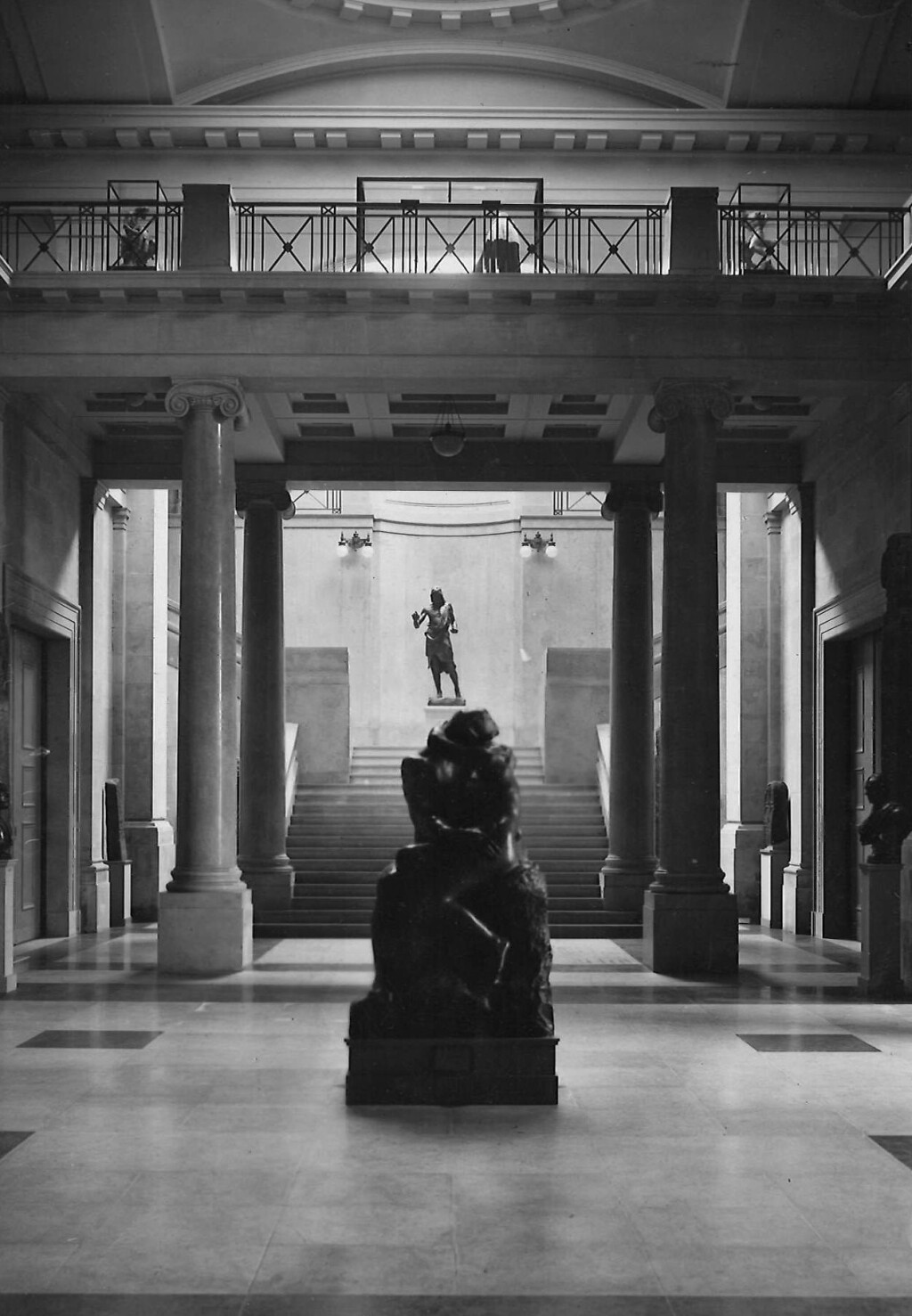 Photograph of the inside of the Main Hall with a grand staircase in the background, large columns supporting the ceiling and sculptures of figures dotted about