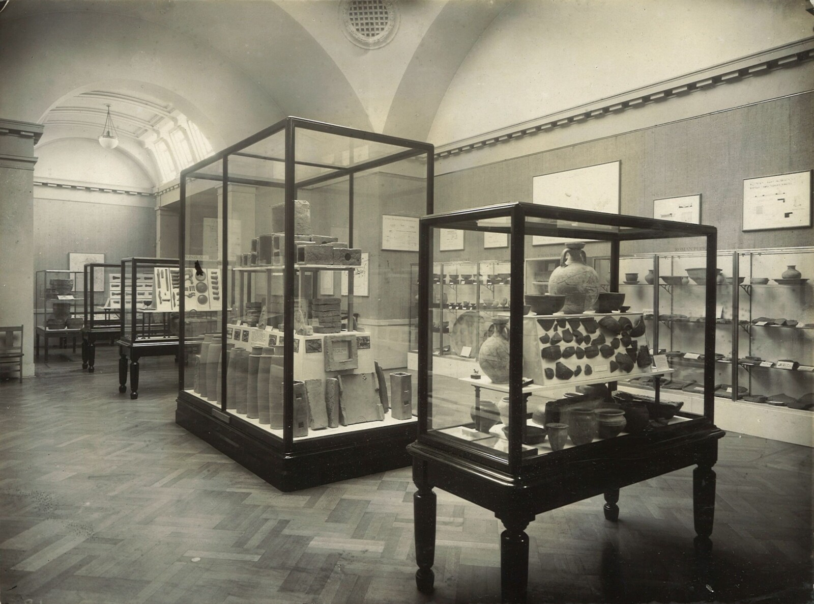 Photograph of the interior of the Archaeology Gallery; there are four large glass cabinets containing Roman pottery standing in the centre of the room