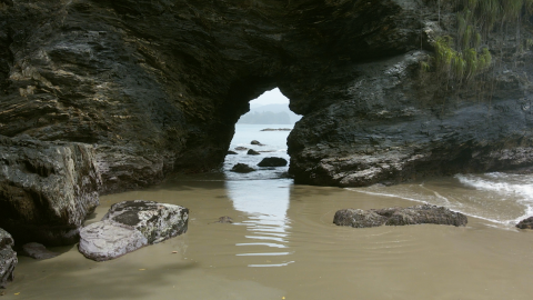 A still from Gesiye's film, showing a beach in Trinidad and Tobago. The perspective of the image looks through a rock formation