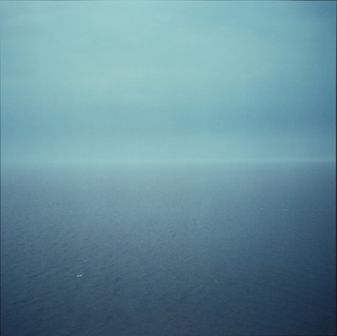 A square photograph with the line where the sea meets the horizon in the centre of the image. The photograph shows a view of Wales from Bristol. The sky and the sea are a beautiful, deep colour blue