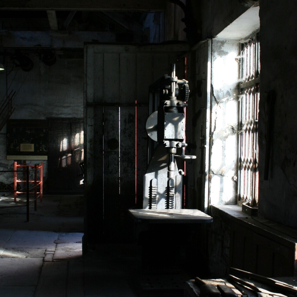 A metal machine is lit up by natural sunlight coming through the shutters on the window. This is an old building and we can see cobwebs around the window itself