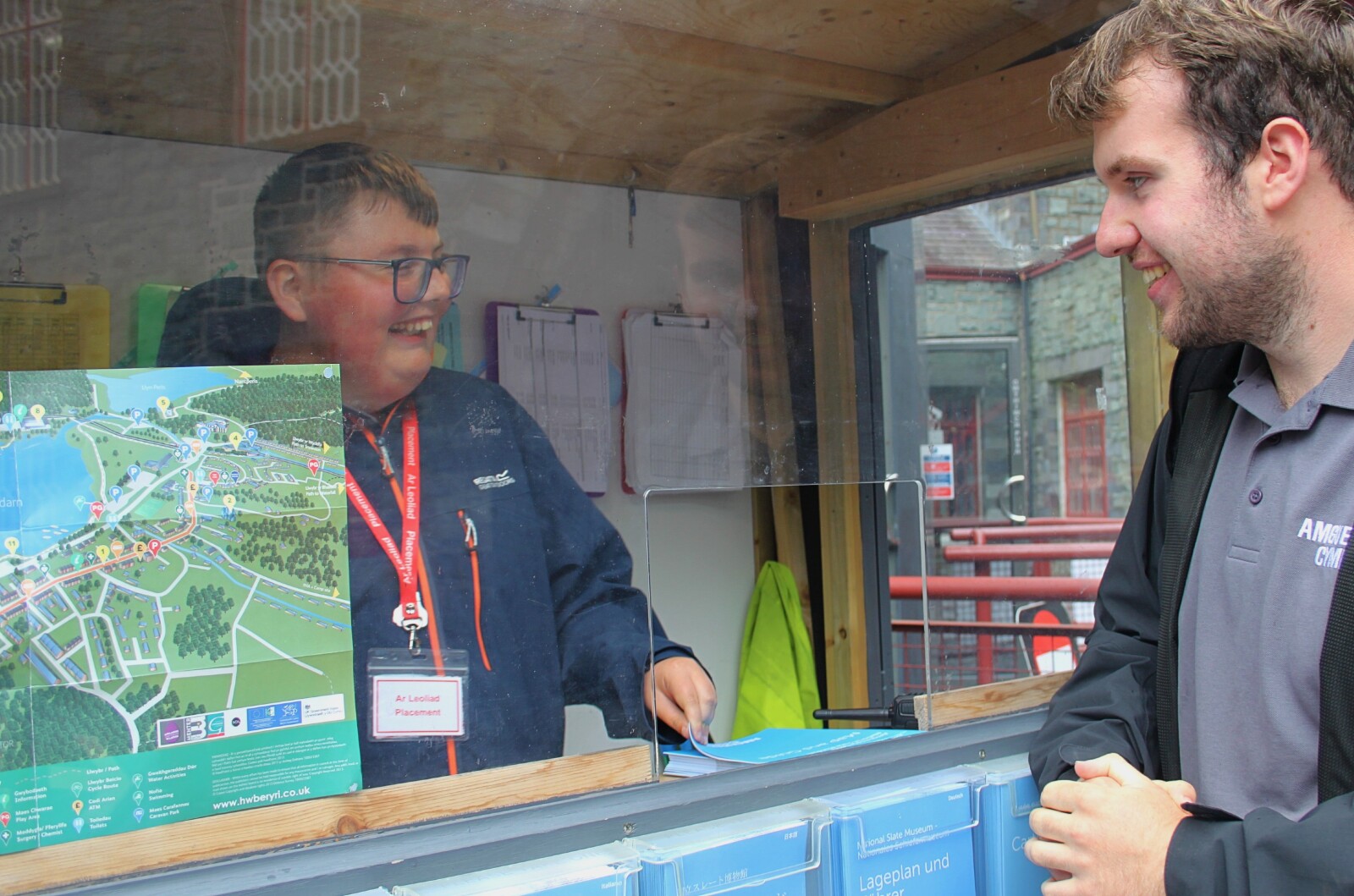 An individual stood inside the welcome hut at the National Slate Museum, smiling while talking to a member of staff.
