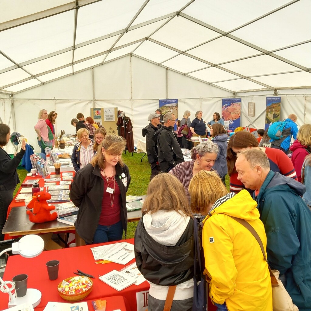 A group of people looking at filled tables within a marquee, the tables include books and leaflets  and in the background there are organisational pop ups