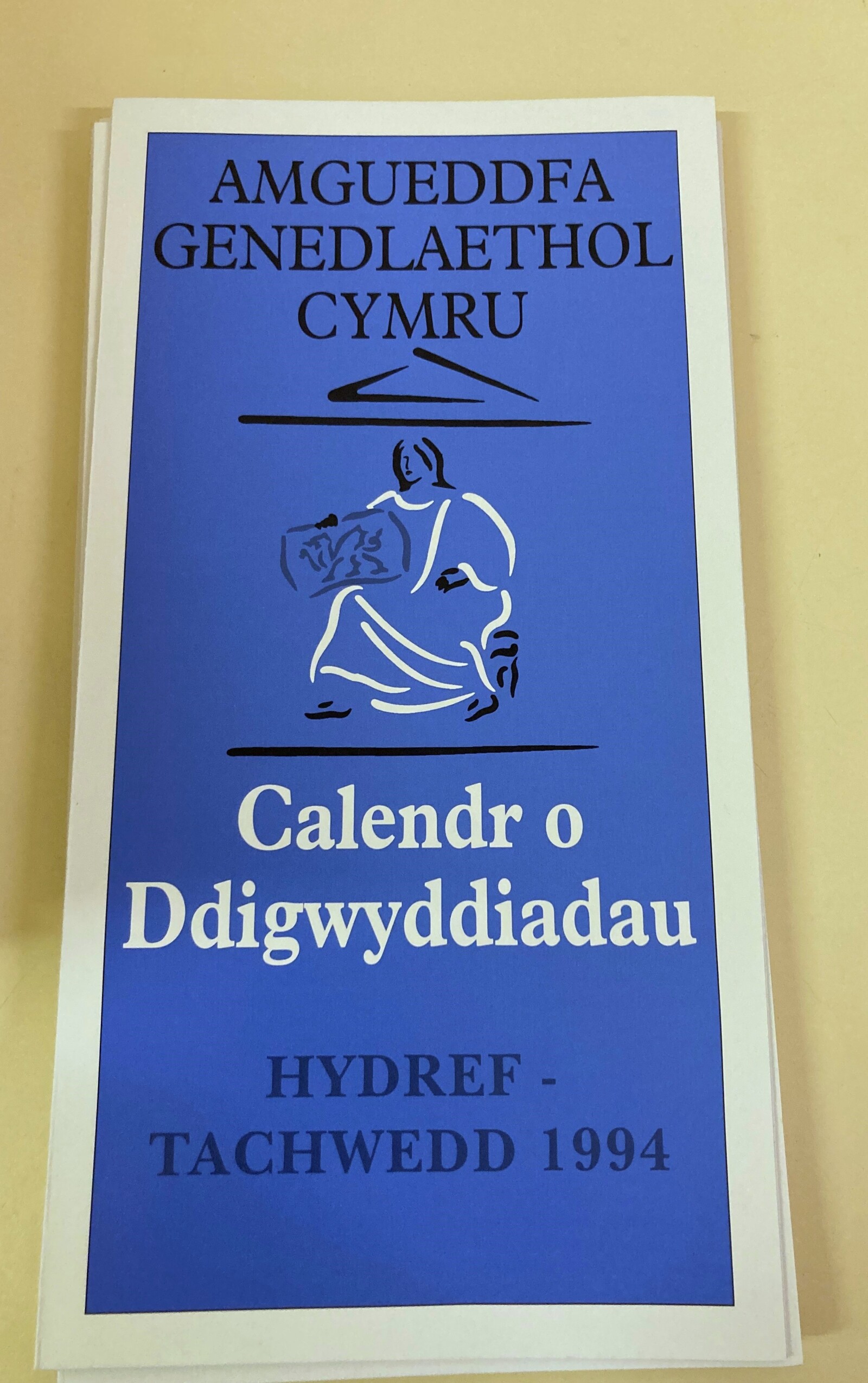 A blue museum leaflet with a line drawing of a woman in white robes holding a welsh flag