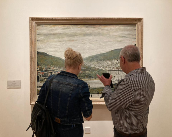 Photo of two people looking at a painting by LS Lowry