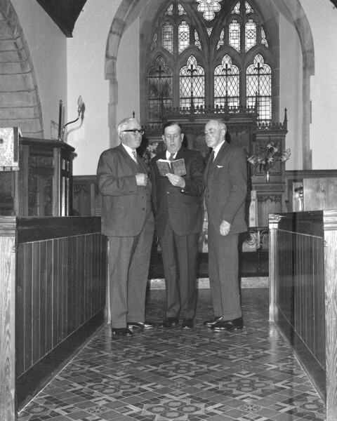 Black and White photograph of three men standing in the isle of a church singing