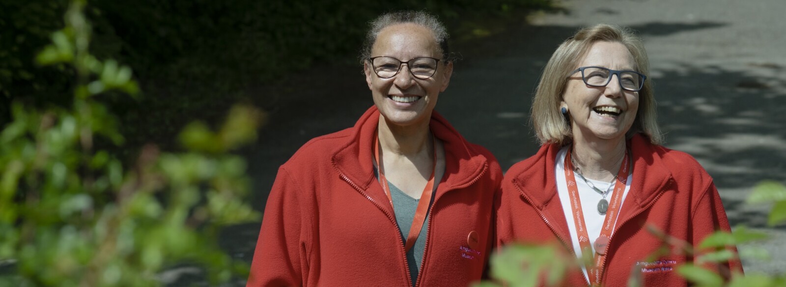 Two volunteers wearing red volunteering fleeces, smiling at the camera. 