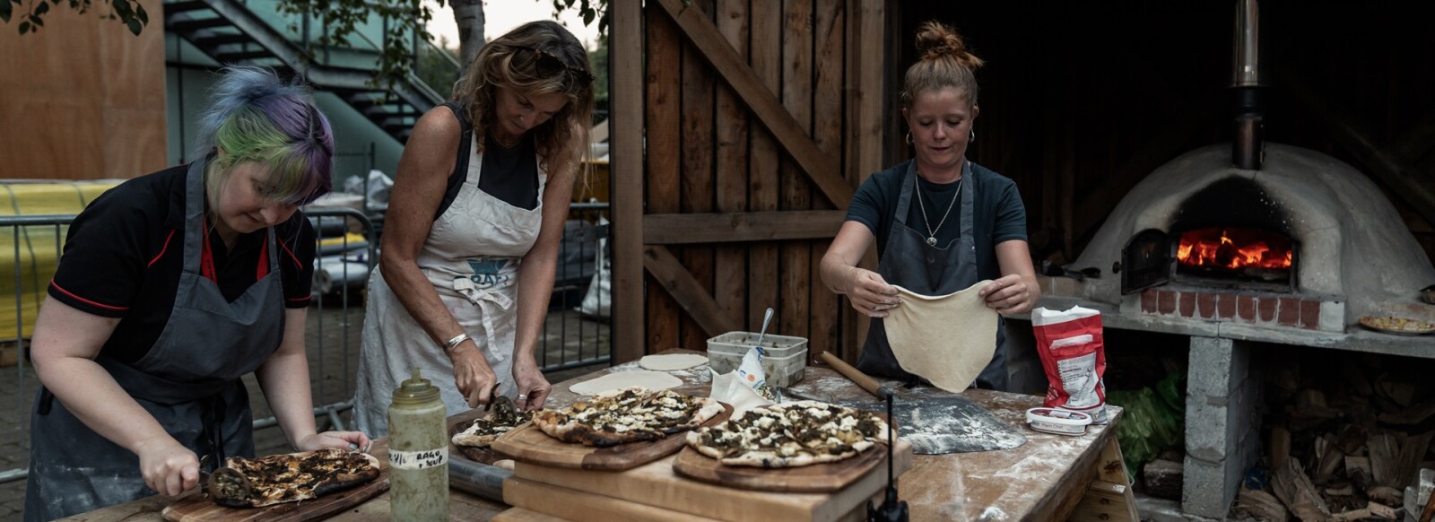 Three people making pizzas in the GRAFT garden pizza oven.
