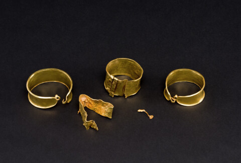 A collection of gold rings on a black counter, there's three rings as well as folded gold and a small spec