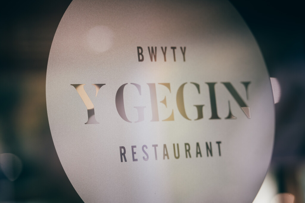 A round sign on a window that reads 'Bwyty Y Gegin Restaurant'