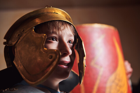 Young boy wearing a Roman helmet.