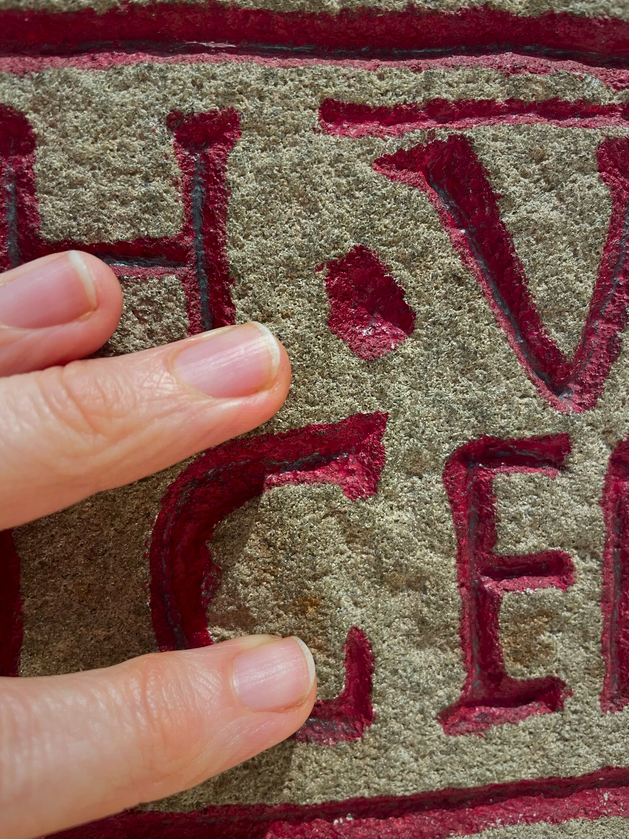 Finger tips touching grey stone engraved with red letters