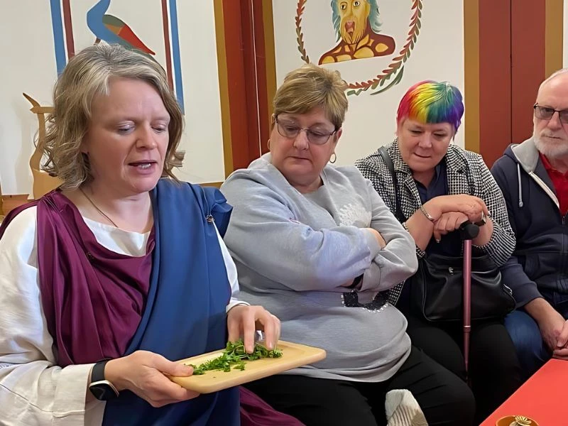 A woman dressed in Roman clothing discussing herbal uses with visitors
