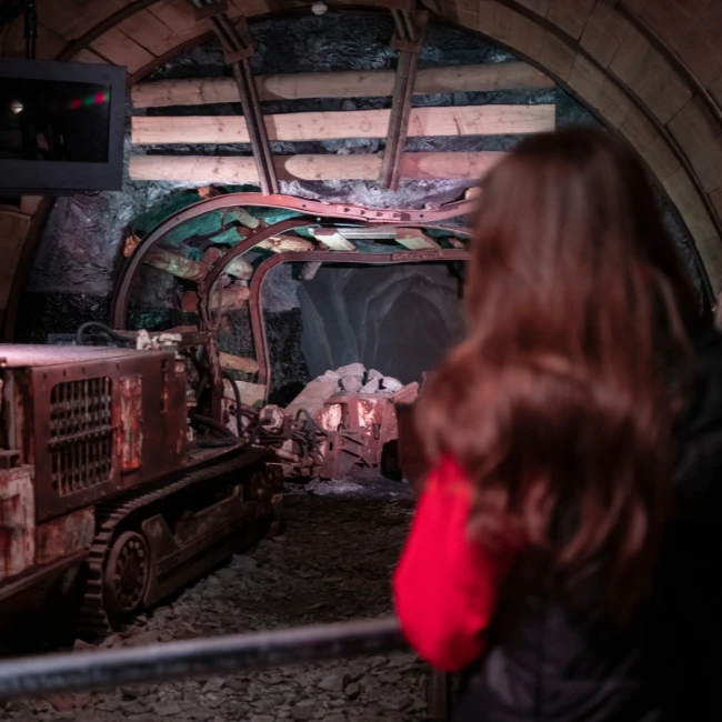 A girl with brown hair and a red sweater looks at a recreation of a collapsing mine tunnel
