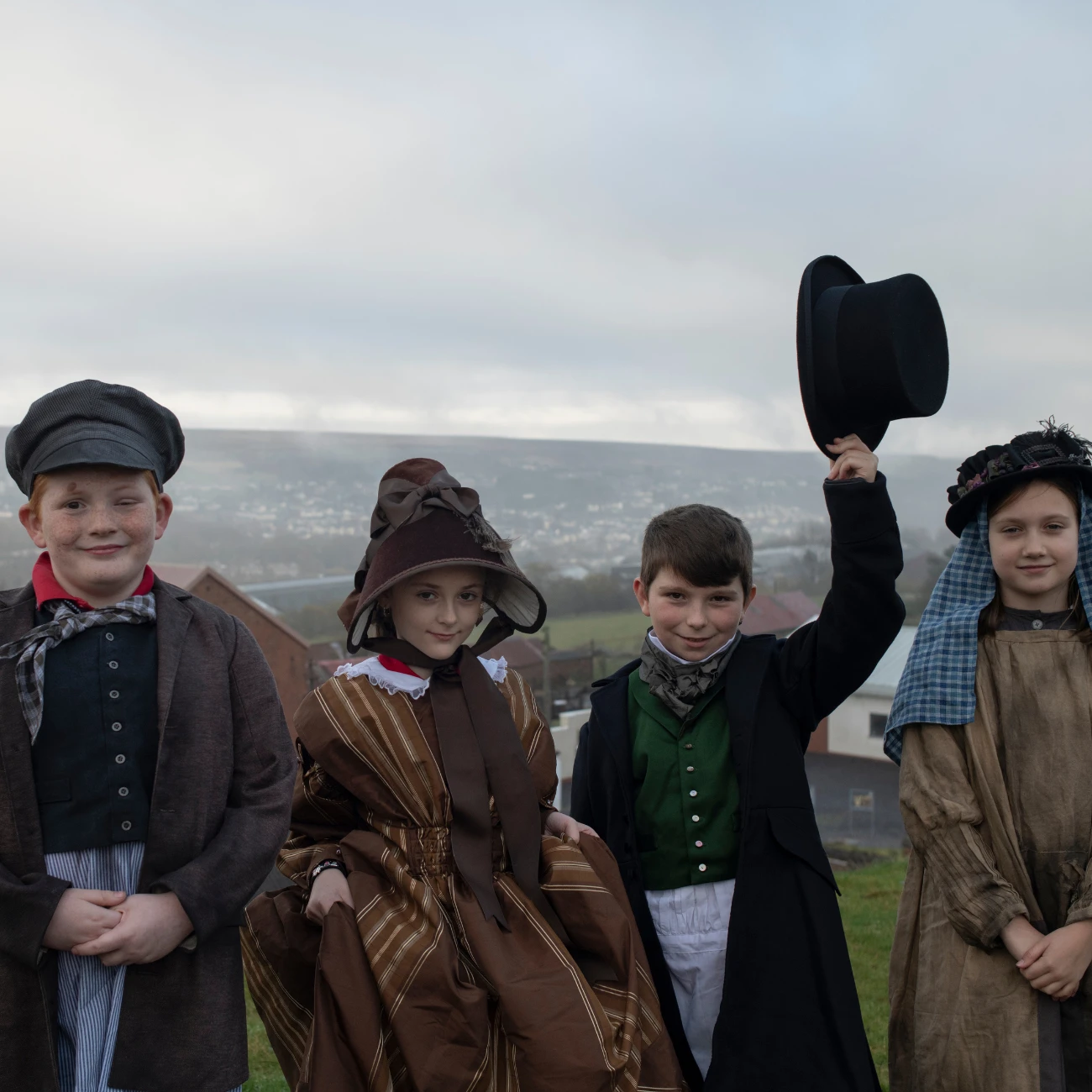 Four pupils dressed in Victorian period clothing. The Big Pit head gear can be seen behind them