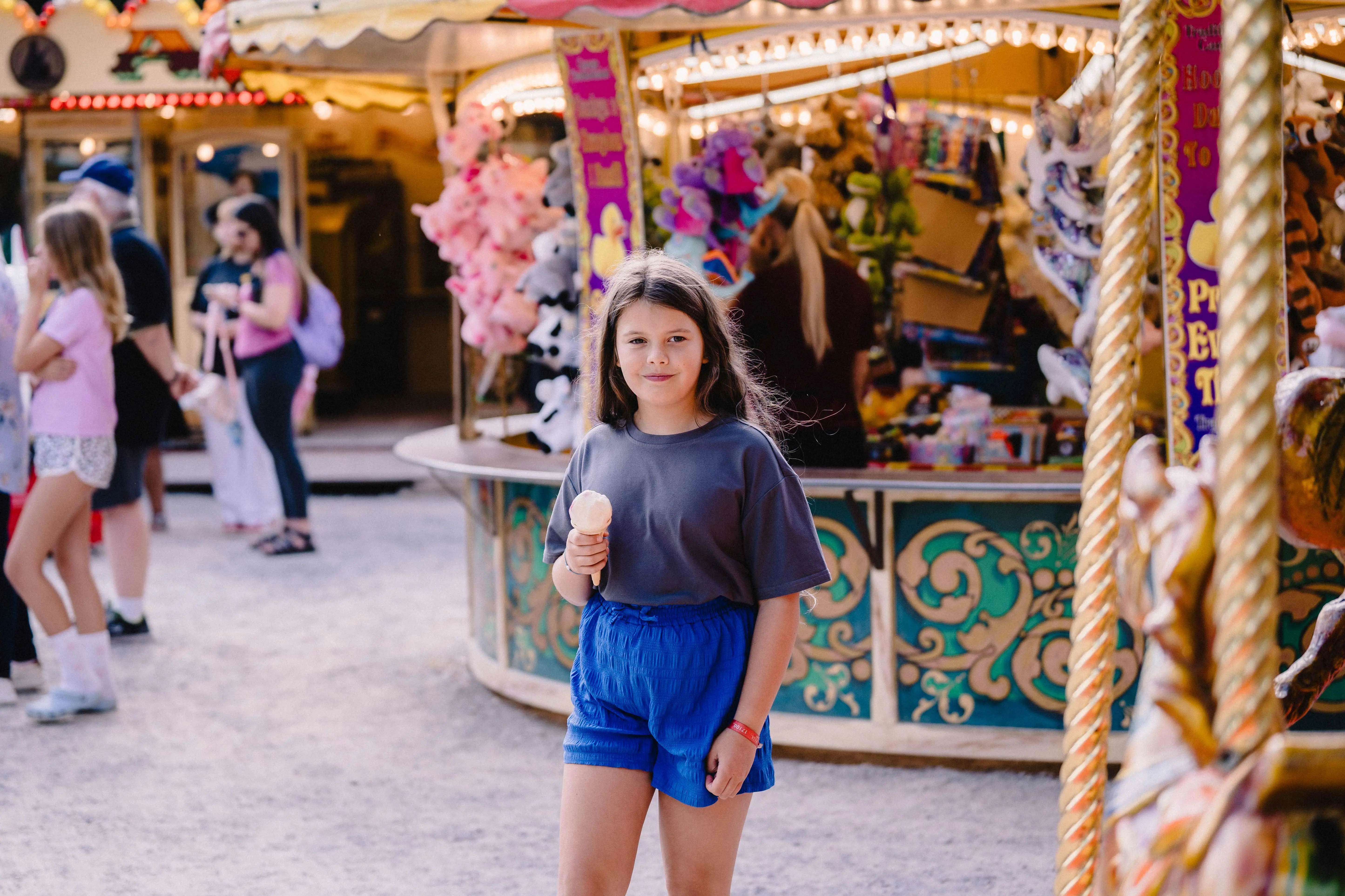 A young girl with long dark hair is eating an ice cream in the traditional fairground 