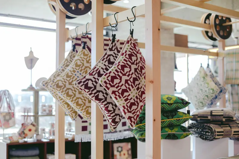 Geometric patterned cushions hanging from a wooden display frame in a shop.
