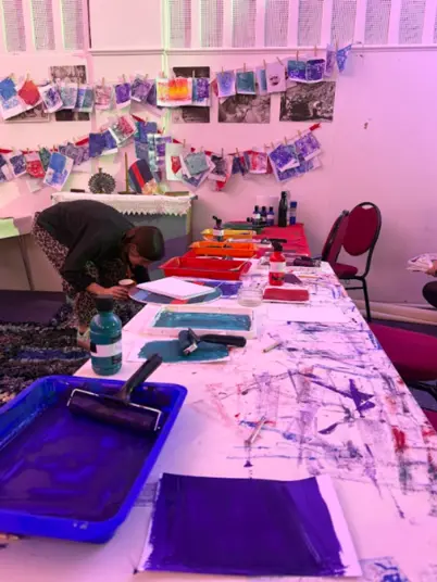 A person preparing for the printing workshop with trays and paint laid out on the tables. In the background some completed work hanging on the wall.