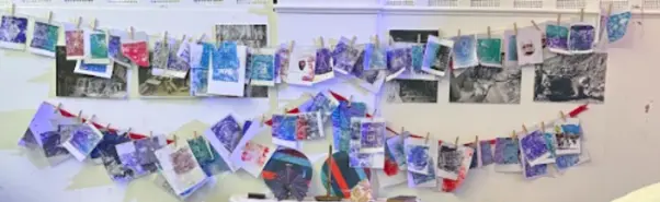 Final prints created by participants in many different colours hanging on a line with pegs holding them in place.
